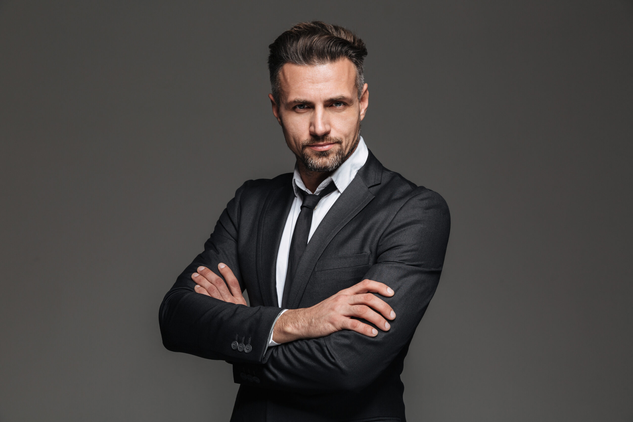 Portret pewnego siebie, elegancko ubranego biznesmena uśmiechającego się pod lekko i patrzącego z wyzwaniem w kamerę. Czy Ty podejmiesz się wyzwania jakim są studia podyplomowe Zarządzanie w Biznesie?